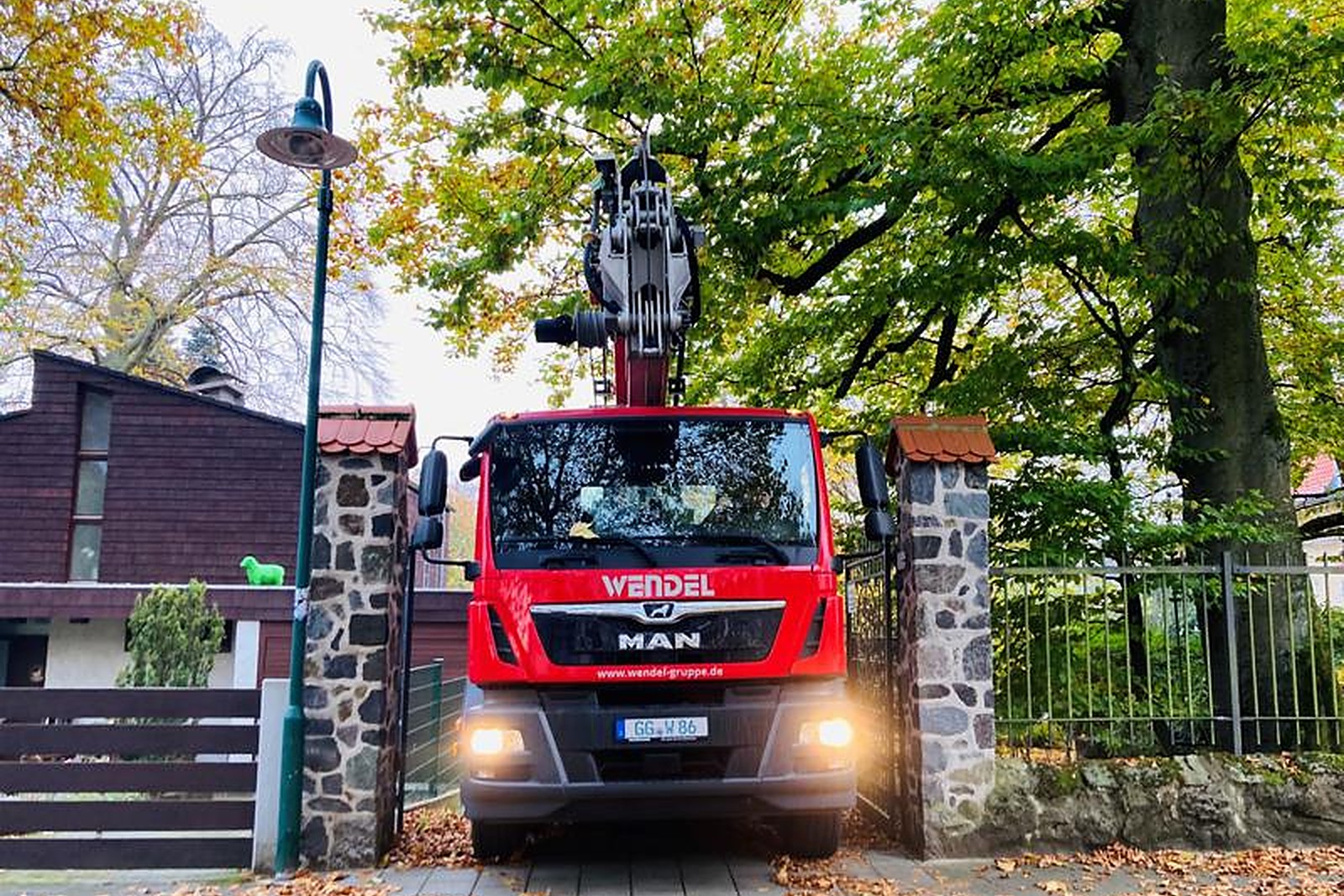 Red Wendel MAN truck-mounted access platform at a residential gate in autumn